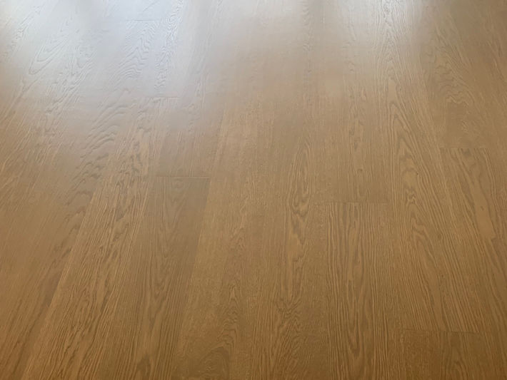 Refinished wide-plank oak hardwood floors in bright Surrey bedroom – high-gloss natural honey tone with mirror-like shine and clean white baseboards.