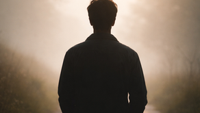 Silhouetted person facing a foggy, sunlit path lined with grass and trees, suggesting quiet resilience.