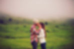 Couple kissing in a misty green field. Man wears a plaid shirt and beanie, woman in a white sweater. Romantic and serene mood.