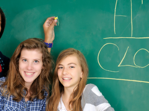 teacher and students smile at chalkboard