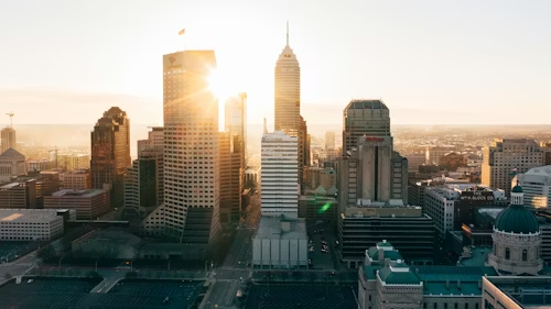 A skyline of tall buildings at sunset, with sunlight gleaming between them. The sky is clear, creating a calm and serene atmosphere.