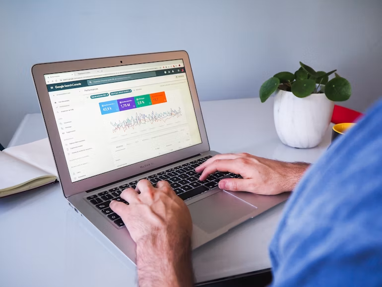 Person typing on a laptop showing Google Search Console analytics, with a potted plant on a clean desk.