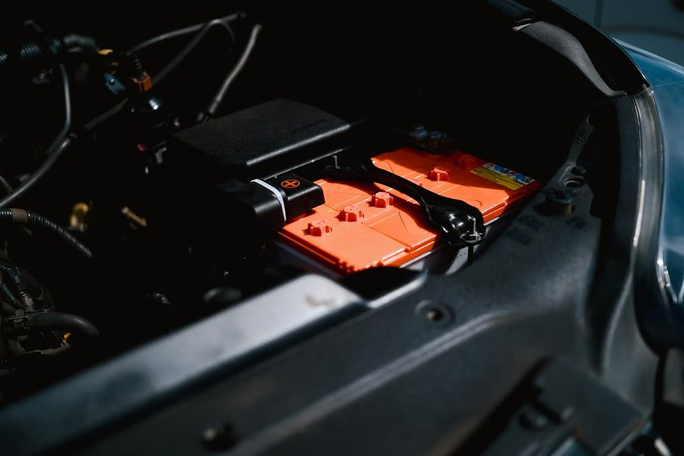 Bright orange car battery secured in a dark engine bay under the hood, with cables and black trim visible.