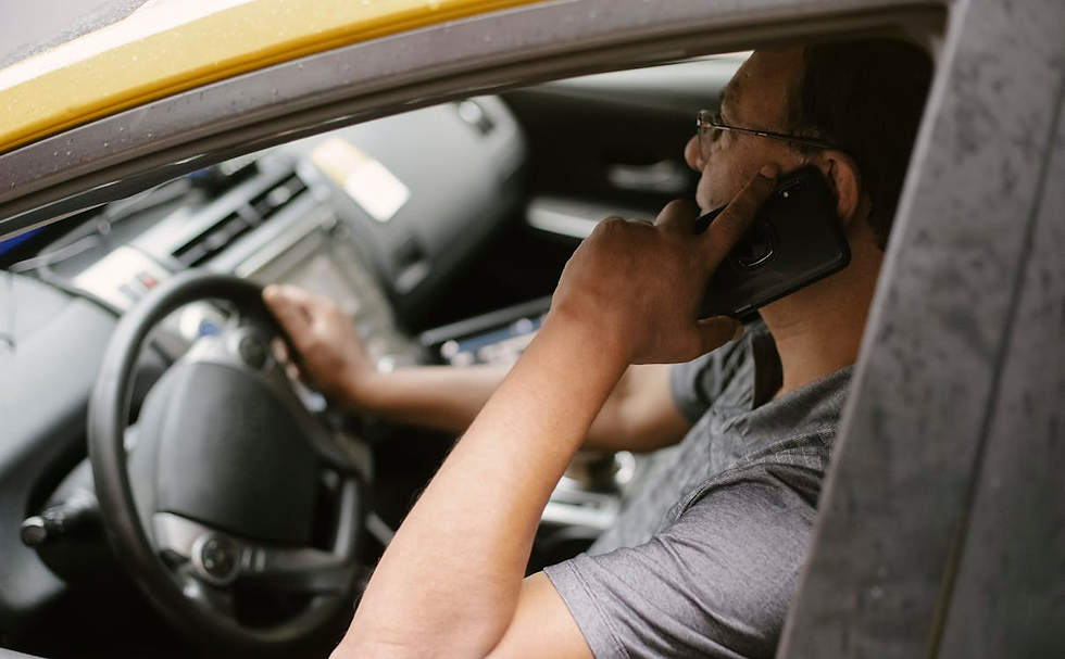 Person driving a car while talking on a smartphone. Interior is visible, with a focus on steering wheel and dashboard. Mood is focused.