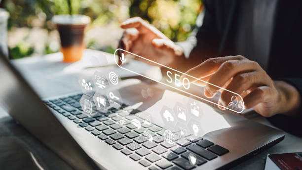 Hands typing on a laptop with "SEO" text overlay and digital icons. Background shows a blurred outdoor scene with natural light.