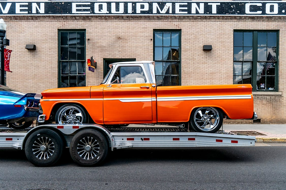 Orange vintage truck on a trailer in front of a brick building with large windows. Sign above reads "EQUIPMENT CO." Street setting.