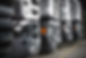 Close-up of parked gray trucks in a row, with one front indicator light glowing amber on a paved lot.