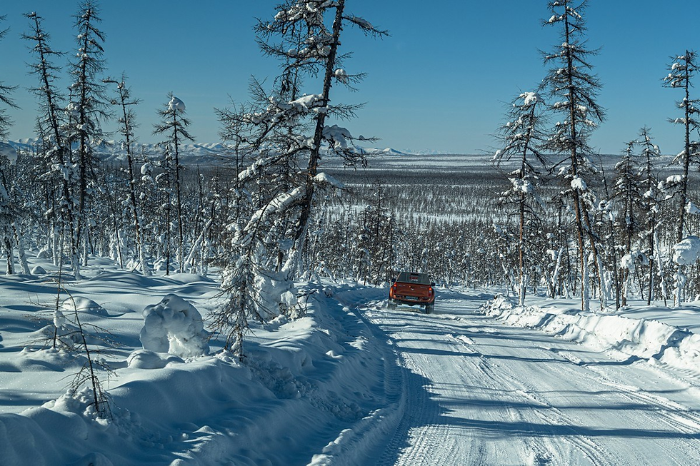 Red truck drives on a snowy road through a forest with frosty trees under a clear blue sky, evoking a sense of isolation and adventure.