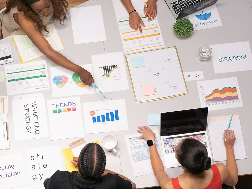 Top view of a diverse team collaborating at a desk with charts, graphs, and laptops. Documents titled "Trends" and "Marketing Strategy" visible.