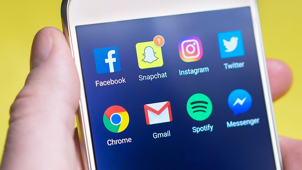 Hand holds smartphone showing Facebook, Snapchat, Instagram, Twitter, Chrome, Gmail, Spotify and Messenger icons on a blue screen.