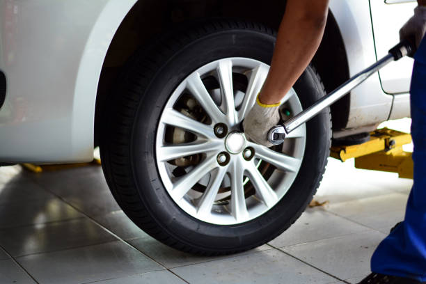 Mechanic tightens a car wheel lug nut with a wrench in a garage, beside a white car on a lift.