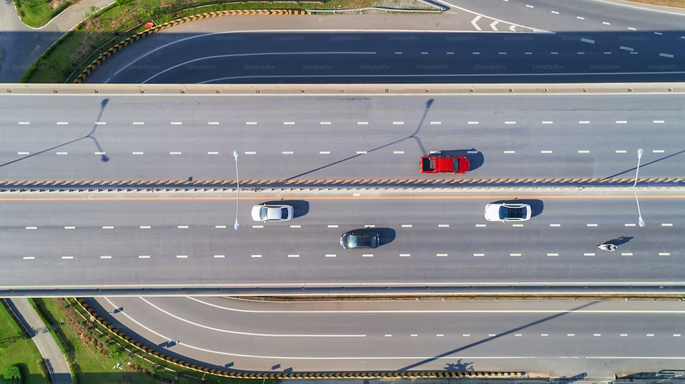 Aerial view of a multi-lane highway with a red car, white cars, and a motorcycle driving under streetlight shadows.