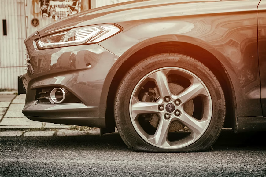 Close-up of a brown Ford car’s front wheel and headlight parked on a street in warm sepia tones.