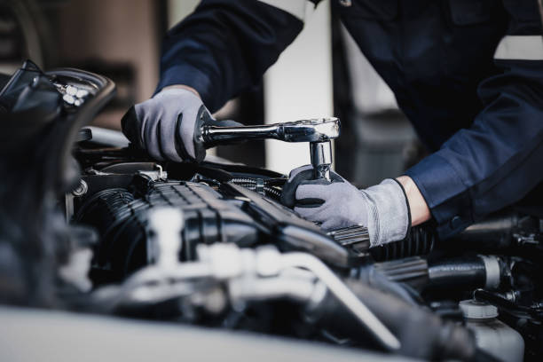 Gloved mechanic tightening a car engine bolt with a ratchet in a workshop, focused and precise.