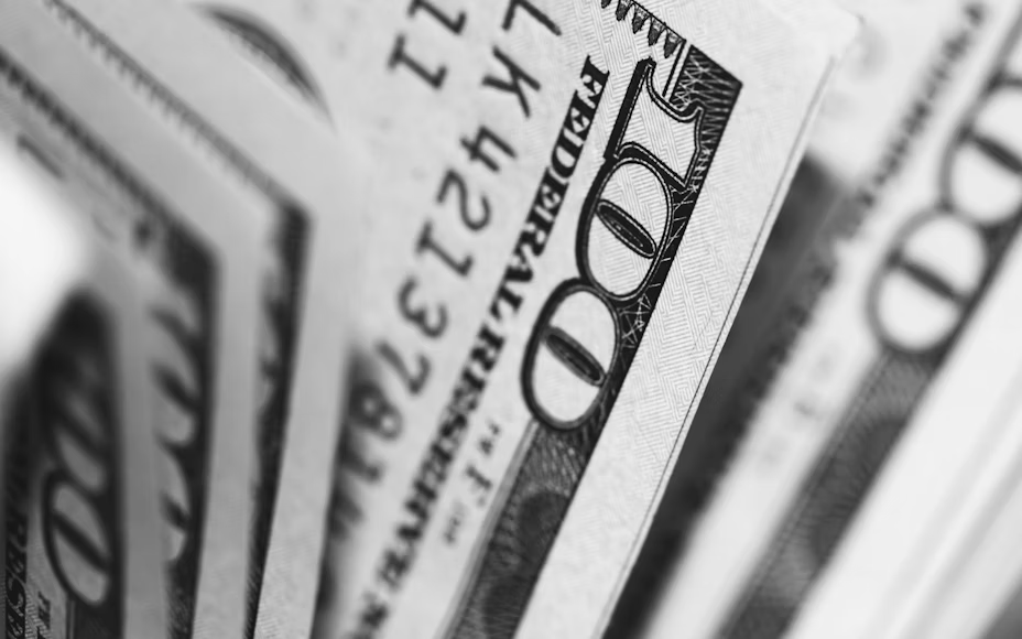 Close-up of several overlapping 100-dollar bills, focusing on the number "100" and intricate line patterns. Black and white.