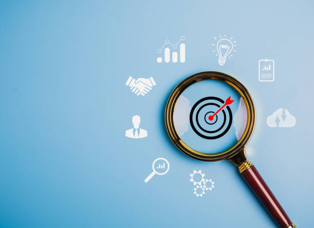 Magnifying glass focuses on a target with an arrow on blue background. Surrounding icons imply business concepts like growth and ideas.