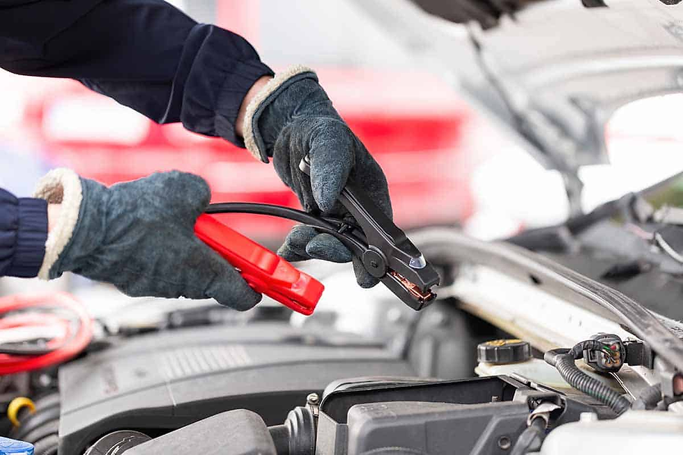Hands in blue gloves use jumper cables to jump-start a car. The hood is open, showing the engine. Red and black cables are visible.