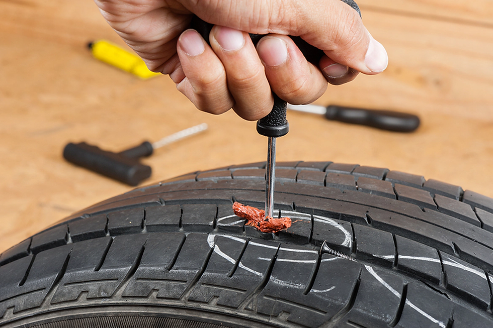 Hand using a tool to repair a punctured tire with a seal plug. Tools are scattered in the wooden background.