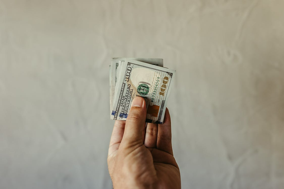 Hand holding several 100-dollar bills against a light textured background, focusing on the currency's details and colorful accents.