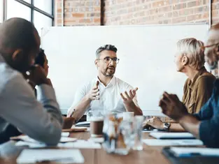 A male leader actively speaking and gesturing to a team of attentive professionals during a meeting in a modern office