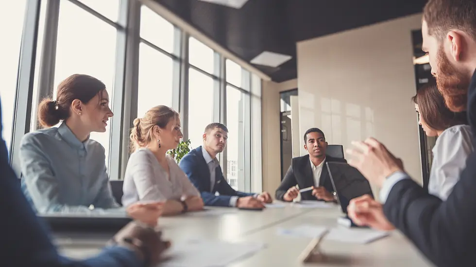 Several people sat around a table in a professional setting, looking at each other whilst talking and listening.