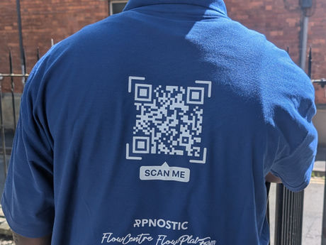 A blue shirt with a white qr code. There is a brick house in the background.