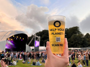 A reusable cup filled with beer, held by someone with a festival stage in the background and a field full of people.