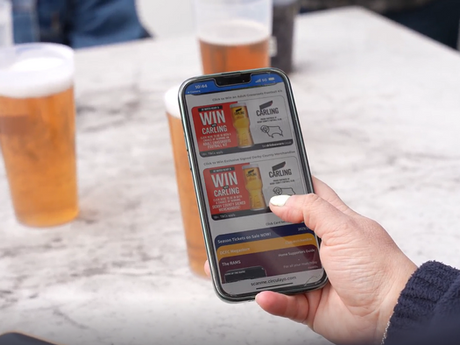 Three reusable cups on a table with a hand holding a mobile phone showing Circulayo Connect with competitions and environmental savings.
