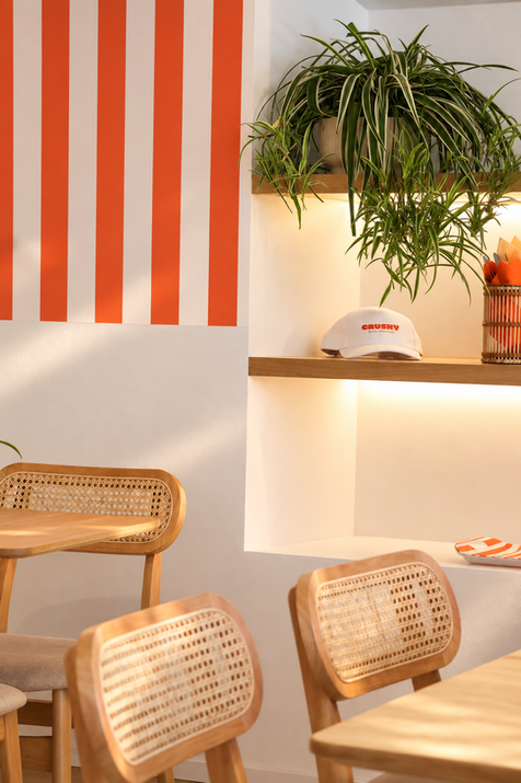 Espace repas du coffee shop CRUSHY à Cogolin avec niches décoratives, chaises en bois et végétation