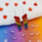 Acrylic rainbow unicorn horn earrings on a colourful background surrounded by mini crystal hearts