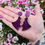 Thumbnail: A pair of glittery purple bat wing earrings being held in front of some colourful flowers
