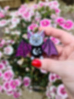An acrylic bat brooch with glittery purple wings being held in front of some colourful flowers