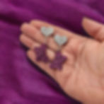 Purple acrylic rainbow butterfly earrings being held in front of a purple background