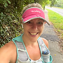 A woman in running kit and a pink baseball cap smiling at the camera