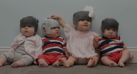 Four babies wearing cranial orthotic helmets