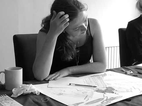 woman sitting at a table looking at a drawing and touching her hair