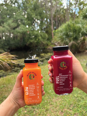 Two hands hold Roots Reboot GLOW and FUEL juice bottles outdoors.