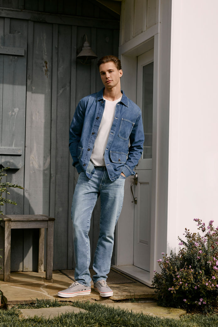Male model in denim and white tee poses confidently outside a modern home, giving off a casual, cool aesthetic.