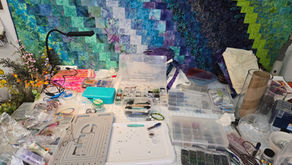 An artist's worktable filled with beads, fibers, fabrics, and tools while creating mixed-media fiber sculptures during a season of healing.