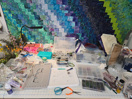 An artist's worktable filled with beads, fibers, fabrics, and tools while creating mixed-media fiber sculptures during a season of healing.