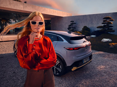 A woman in sunglasses posing next to a sleek car, exuding confidence and style.