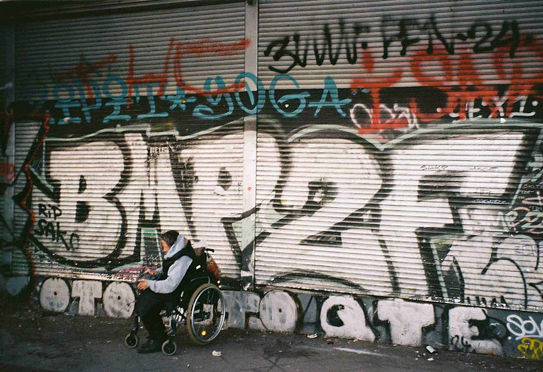 analoge Fotografie einer Frau im Rollstugl vor einer Graffitiwand