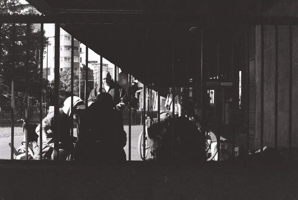 Silhouetten von Menschen in überdachter Wartehalle eines Bahnhofs, dramatisches Gegenlicht, urbane Straßenfotografie