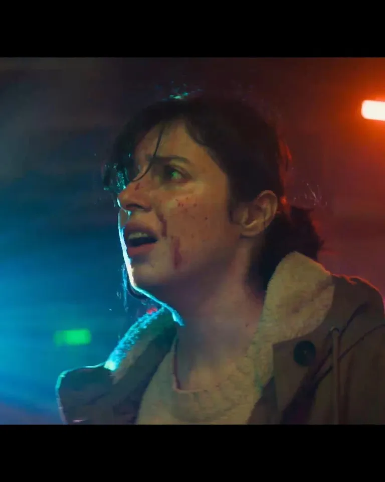 Film still of a woman with red marks on her cheek under blue and red lighting.
