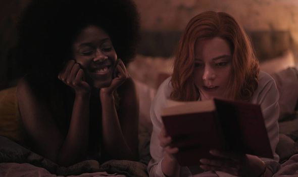 Elizabeth and her friend, Jolene, lie across a bed reading a book, Elizabeth looks in wonder while Jolene smiles widely.
