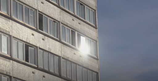 A plain block of flats against a blue sky, the sunlight is glinting off the windows