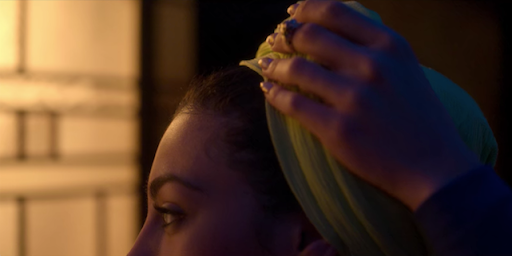 A still from Netflix's Elite: Nadia is removing her headscarf, we can only see her eyes and the top of her head.
