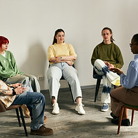 Group of diverse young adults sitting in circle while professional therapist leading sessi