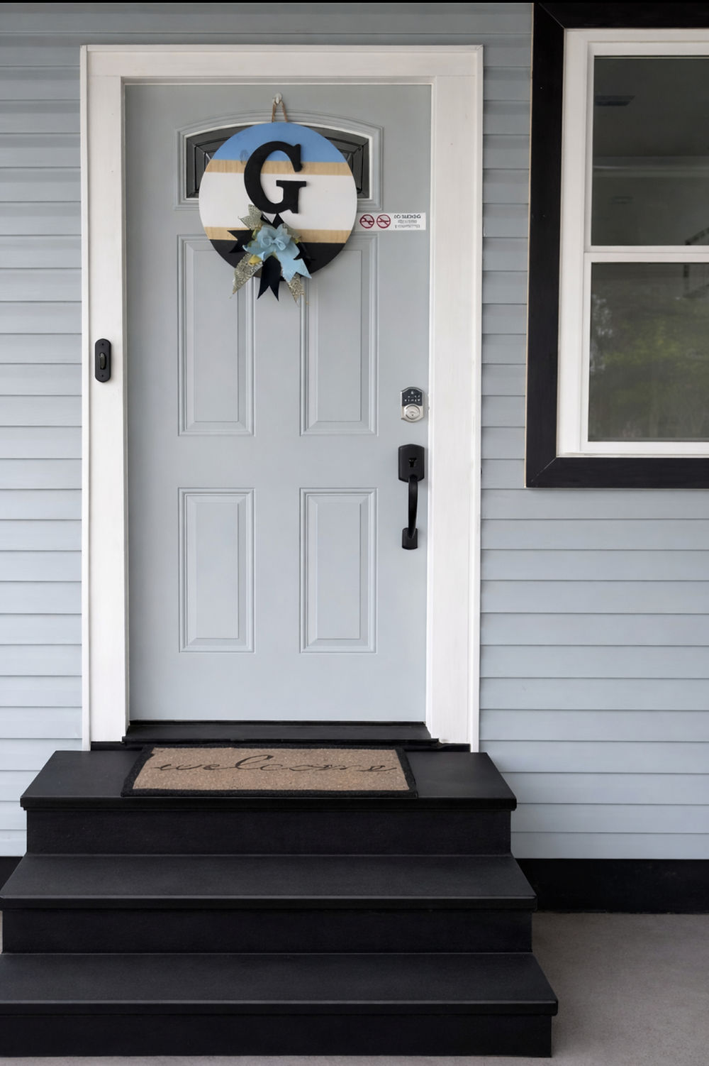 Light blue front door with black steps and a welcome mat