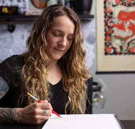 Cherise a heavily tattooed woman tattooer sitting at her work station drawing tattoo designs